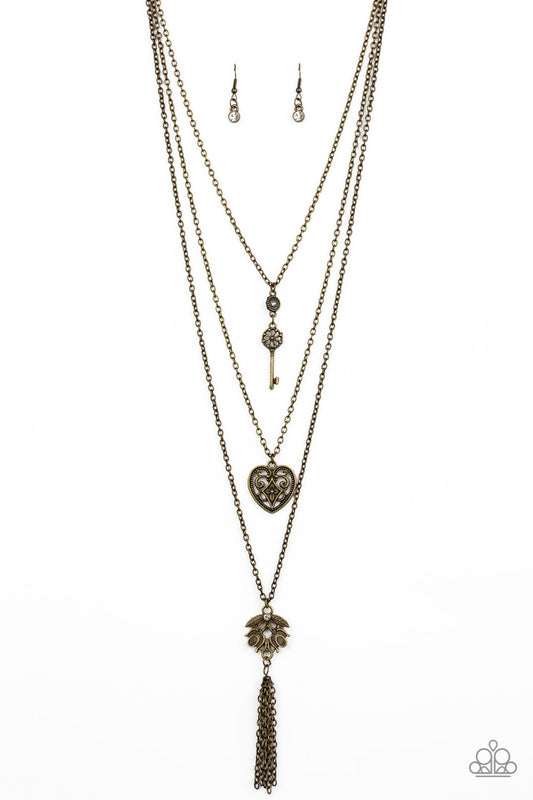 Paparazzi Necklace - A shimmery brass key, heart-like frame, and leafy brass pendant layer down the chest in a whimsical fashion. Infused with a playful tassel, glittery white rhinestones adorn the upper and lowermost frames for a sparkling finish.