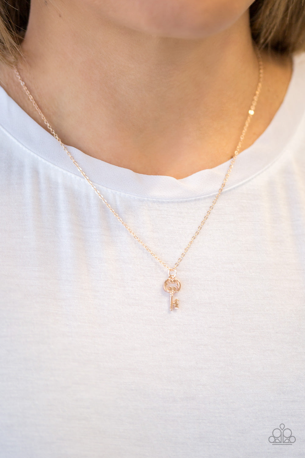 Paparazzi rose gold key swings from the bottom of a shiny rose gold chain, creating a whimsical pendant below the collar. Features an adjustable clasp closure.