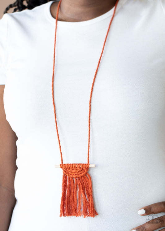 Orange cording delicately wraps around a dainty wooden dowel, knotting into a tasseled macrame centerpiece at the bottom of a dramatically lengthened display. 