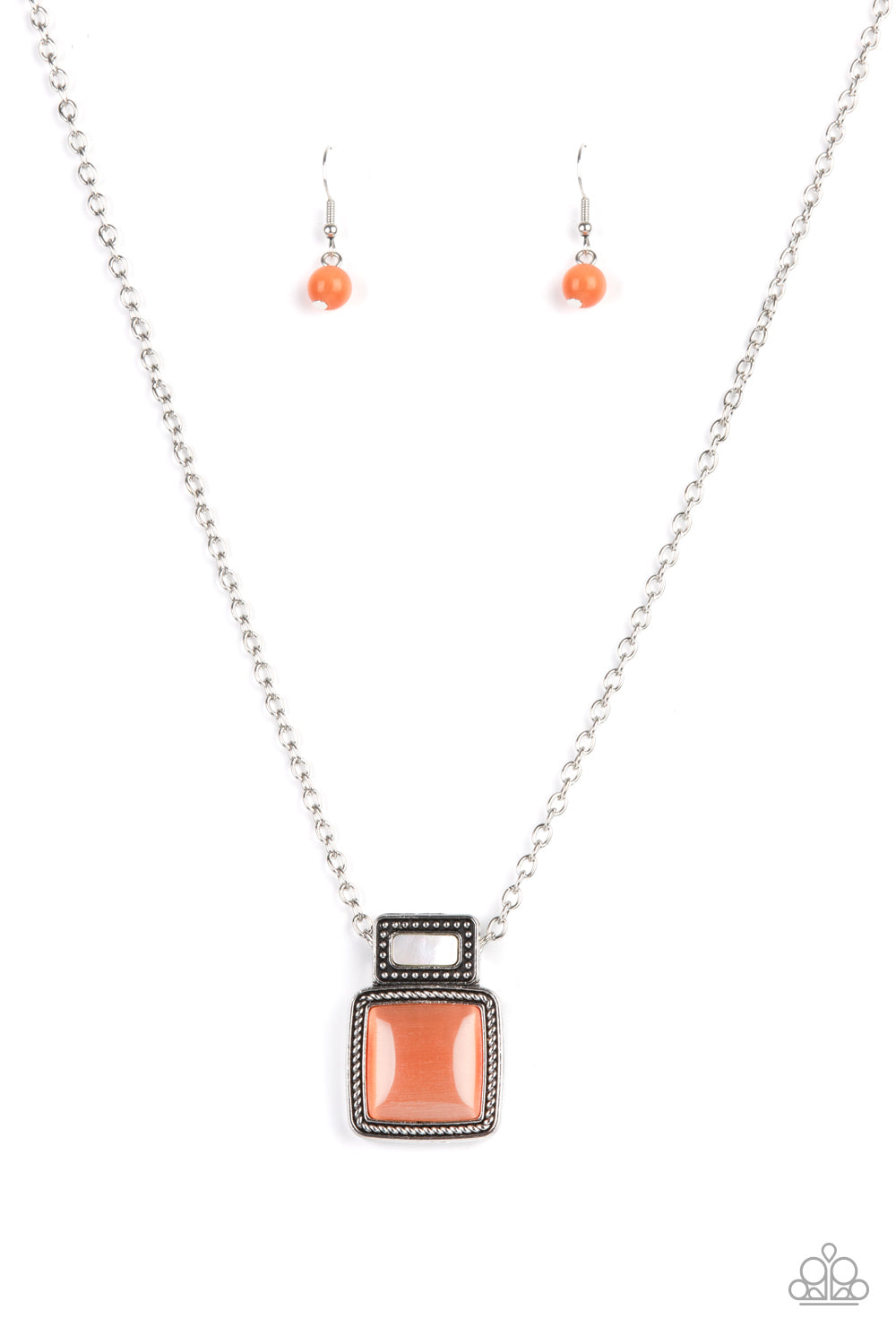 A shell-like accent is pressed into the center of a studded silver frame that sits atop a silver rope-like frame that is dotted with a square orange cat's eye stone. 